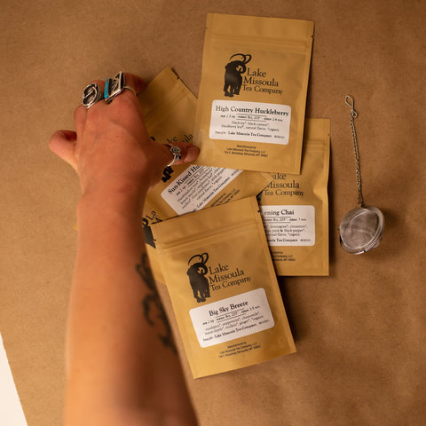 Hand arranging packages of Lake Minnowa Tea Company on a brown surface.
