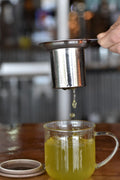 Glass cup with brown lid filled with Lake Missoula Tea Company Internal Bliss #2 Regular Move Blend herbal tea.