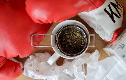 Lake Missoula Tea Company's "Beat the Snot Out of You" sinus tea, showing a tea bag steeping in a cup with fresh herbs and tea leaves.