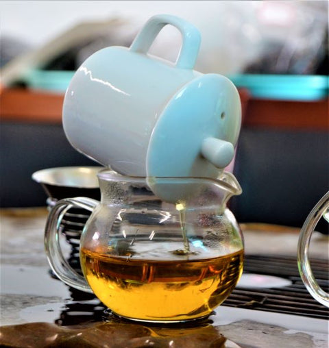 Fresh brewed Dragonwell green tea in a glass cup, showcasing vibrant green leaves and steaming hot beverage from Lake Missoula Tea Company.