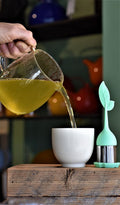 Green Ginger Jazz tea from Lake Missoula Tea Company being poured into a cup with a leaf infuser.