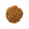 Cup of Lake Missoula Tea Company's Turmeric Ginger Twirl tea with vibrant ginger and turmeric root slices on a rustic surface.