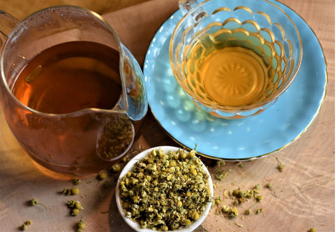 Top view of a cup of chamomile tea on a blue plate, showcasing dried chamomile flowers and a calming presentation.