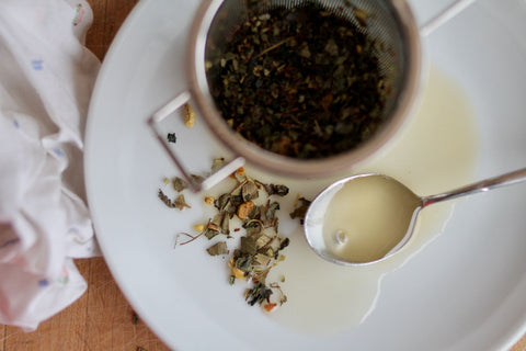 A cup of herbal tea labeled "No Thyme for Cold & Flu" by Lake Missoula Tea Company, with fresh herbs and honey on a wooden table.