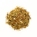 A cup of Lake Missoula Tea Company's Skin Glow herbal tea with fresh herbs and flowers in a glass teapot on a wooden table.