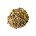 A cup of Lake Missoula Tea Company's Cycle Goddess herbal tea in a white mug on a wooden table, with tea leaves and herbs visible.