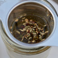 Cup of Lake Missoula Tea Company's Licorice Mint tea in a white mug, with fresh mint leaves and licorice root visible beside it.