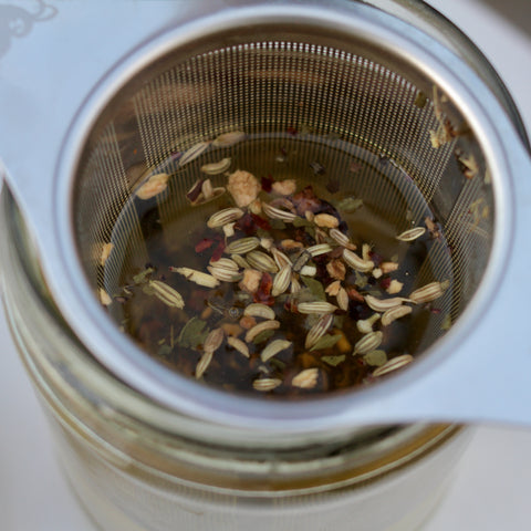 Cup of Lake Missoula Tea Company's Licorice Mint tea in a white mug, with fresh mint leaves and licorice root visible beside it.