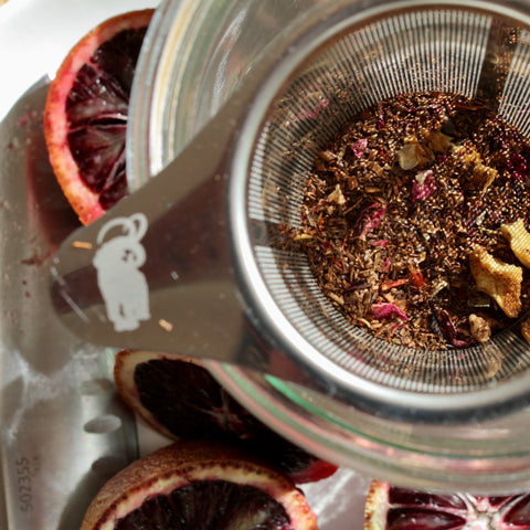 Fresh brewed Blood Orange Rooibos tea in a clear glass cup, highlighting its vibrant orange color and herbal tea leaves.