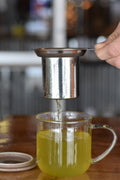 Lake Missoula Tea Company Uplift tea in a clear glass drip cup, showcasing vibrant green tea leaves and fresh infusion.