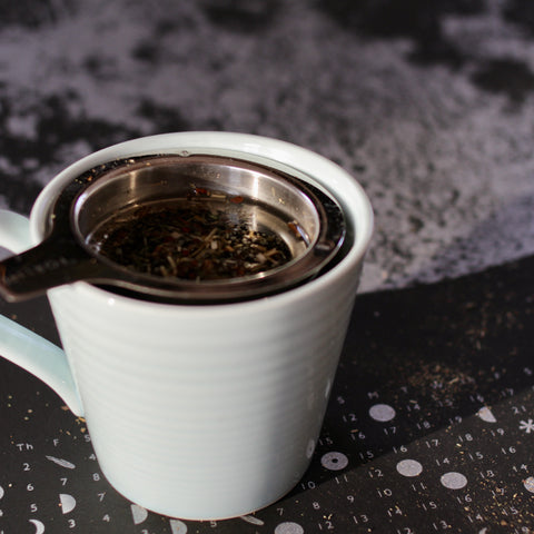 Cup of Cycle Goddess green tea from Lake Missoula Tea Company with green hair-inspired tea leaves in a clear glass.