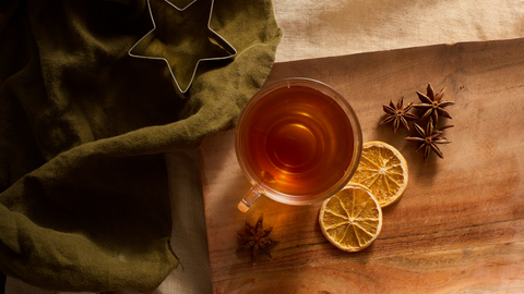 Fall brewed tea with star anise and citrus chips, wood and linen background for a cozy cup.