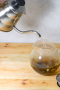 Hario Buono kettle with glass body and metal lid, used for pouring hot water in tea preparation, by Lake Missoula Tea Company.