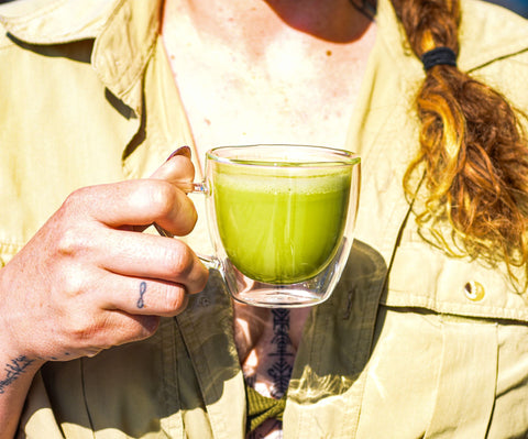 Person holding a cup of Lake Missoula Tea Company's instant matcha tea, showcasing the vibrant green powdered tea in a white cup.
