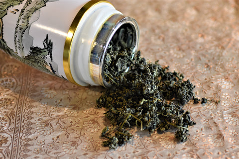 Loose leaf Jiaogulan tea, also known as Immortality Herb, in a container, displayed alongside its dried leaves for brewing.
