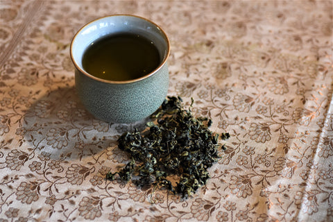 Cup of Jiaogulan Immortality Herb tea in a glass mug, showing fresh green Jiaogulan leaves and brewed herbal tea.