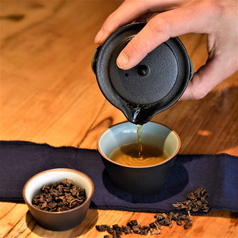 Pouring cup of Lake Missoula Tea Company's Java Oolong Medium tea, showcasing loose tea leaves and brewed tea in a clear cup.