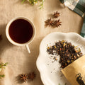 Cup of brewed tea beside a dish of loose leaf tea and star anise on a linen cloth