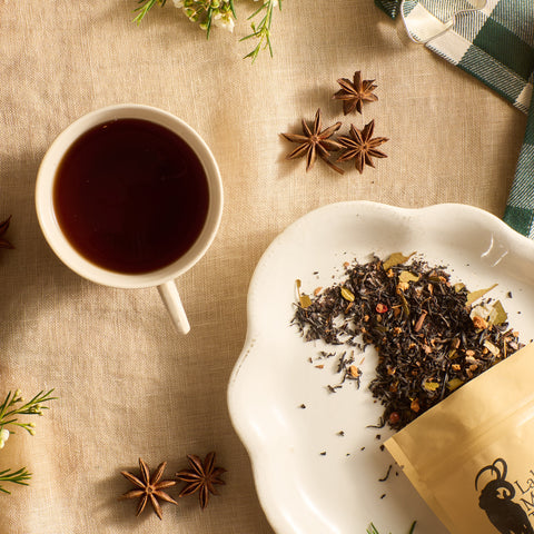 Cup of brewed tea beside a dish of loose leaf tea and star anise on a linen cloth