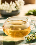 Glass cup of brewed Mountain Winter Berry tea on a green plaid cloth with white flowers behind