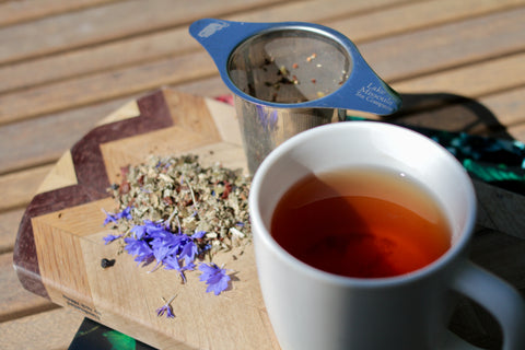 A cup of Sun-Kissed Huckleberry tea from Lake Missoula Tea Company with fresh huckleberries and cornflowers on a summer picnic table.