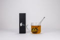 Glass mug with tea and a tea bag, next to a black box with branding on a white background