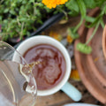 A cup of brewed Nandi Hills Kenyan Black Tea from Lake Missoula Tea Company on a saucer with tea leaves nearby.