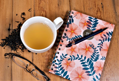 A cup of Yerba Lemon Basil tea from Lake Missoula Tea Company, with a green tea infusion, surrounded by a planner, pen, and glasses.