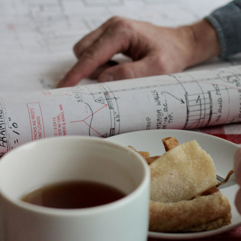 Hands holding a cup of Lapsang Souchong tea from Lake Missoula Tea Company, with apple pie decorations in the background.