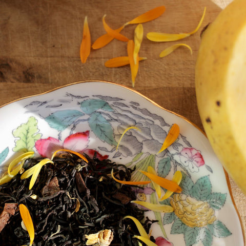 Fresh Mango Love Not War tea from Lake Missoula Tea Company with vibrant marigold flowers in a clear glass cup.