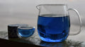 Blue glass carafe and cup with butterfly pea flower tea by Lake Missoula Tea Company, set near a window.