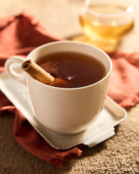 Brewed cup of christmas tea caffeine free in white mug with cinnamon stick.