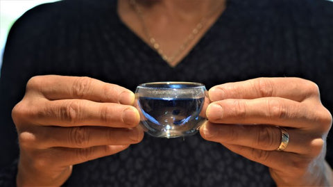 Fingers holding a blue glass cup of Butterfly Pea Flower tea from Lake Missoula Tea Company, vibrant blue color and floral infusion visible.