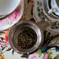 Green-haired woman holding a cup of Lake Missoula Tea Company herbal tea, showcasing vibrant hair and a peaceful expression.