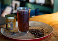 Chilled Gin & Cream Rooibos tea served in a glass, with loose tea leaves and honey spoon on a wooden surface.