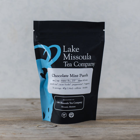 Two ounces of Lake Missoula Tea Company's Chocolate Mint Puerh tea leaves in a clear bag, showing dark tea leaves with mint accents.