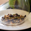 Cup of Stress Less herbal tea by Lake Missoula Tea Company in a white teacup with tea leaves and herbs visible.