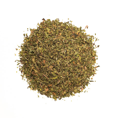 Fresh brewed Lake Missoula Tea Company peppermint tea in a clear glass cup with mint leaves on a wooden table.