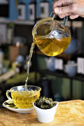 Pouring Heritage Green tea from Lake Missoula Tea Company into a cup, showcasing its vibrant green color.