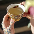 Hands holding a butterfly-shaped tea cup with colorful flowers, showcasing Lake Missoula Tea Company's "A Few of My Favorite Things" tea.