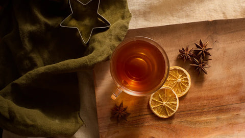 Fall brewed tea with star anise and citrus chips, wood and linen background for a cozy cup.