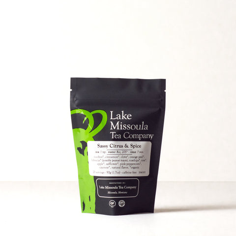 Two ounces of Lake Missoula Tea Company's Sassy Citrus & Spice tea in a clear bag with a label and a citrus fruit beside the package.