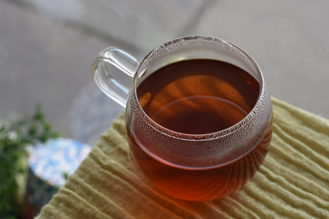 Glass cup of brewed Rooibos Rose tea from Lake Missoula Tea Company, showing vibrant red herbal tea with rose petals.