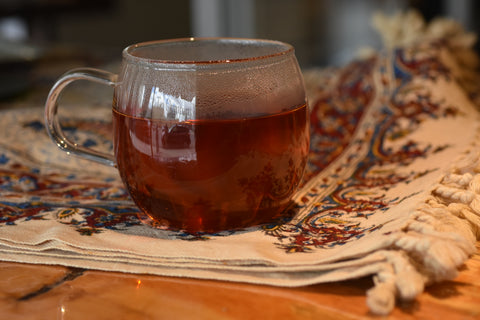 Cup of Rugger's Rooibos tea from Lake Missoula Tea Company on fabric, showcasing vibrant reddish-brown tea leaves and brewed tea.