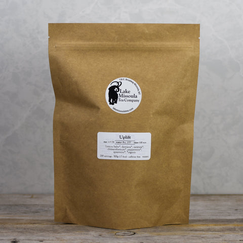 Lake Missoula Tea Company Uplift tea in 500g package, showing the colorful tea blend in a clear container with fresh herbs and flowers.