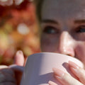 Woman enjoying a cup of Jurassic Ginger Green tea by Lake Missoula Tea Company, with a pink cup and serene background.